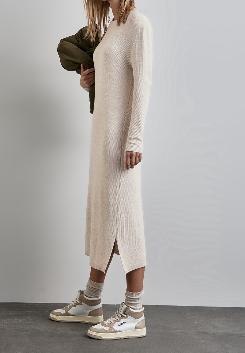 Robe en tricot beige à côtes longues avec fentes sur les côtés, assortie à des baskets montantes blanches et beiges et des chaussettes légères grises à motifs.
