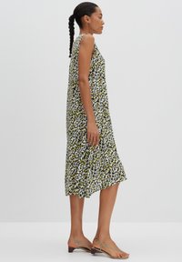 Florales Midi-Kleid in Schwarz, Grün und Weiß mit lockerer Passform, ärmellosem Design und ausgestelltem Saum. Tragen mit flachen Riemchensandalen.