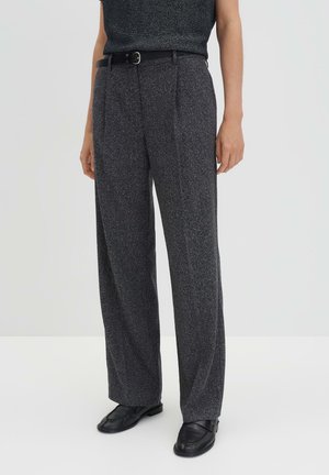 Grijze broek met wijde pijpen en een gestructureerde afwerking, voorzien van voorplooien en een zwarte riem. Gepaard met zwarte schoenen.