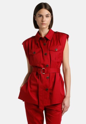 Rood riemloos hemdjurkje met twee borstzakken, knoopsluiting en schouderkapjes; gemaakt van een soepele stof met een getailleerde taille.