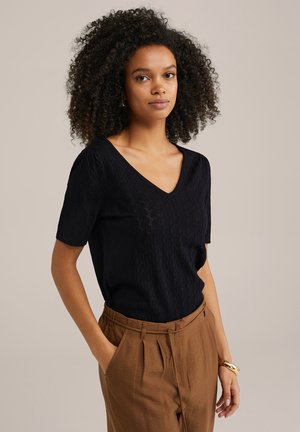 Top nero a maniche corte e scollo a V con un motivo testurizzato, abbinato a pantaloni marroni a vita alta. Design semplice senza accessori o dettagli.