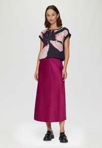 Top floreale blu scuro e rosa, abbinato a una gonna midi magenta. Il modello indossa mocassini neri in vernice. Design semplice e rilassato.