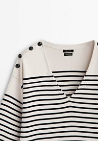Pull en V à rayures blanches et noires avec des boutons noirs le long d'une épaule, en 100 % coton.