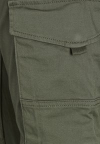 Osasto khaki cargo-housuja, jossa on suuri läppätasku. Materiaali on kestävä, sileä tekstuuri ja näkyvät ompelusaumat.
