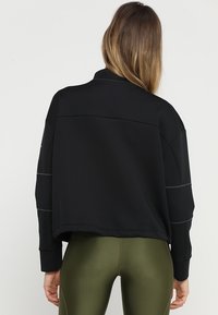 Svart cropped sweatshirt med långa ärmar, har en avslappnad passform, sömdetaljer och en mjuk textur, i kombination med olivgröna leggings.