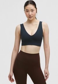 Donkerblauwe sportbeha met een V-halsontwerp, brede bandjes en een gladde textuur, gecombineerd met hooggetailleerde bruine legging.