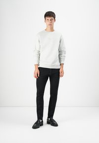 Light gray sweatshirt with crew neck, ribbed cuffs, and logo. Paired with slim-fit black jeans and black leather shoes. Simple design.