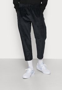 Tmavě námořnické kordové kalhoty se stahovacími pasem, tapered nohavicemi a jemným vertikálním žebrováním. Doplněné o bílé tenisky.