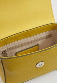 Žlutá kožená kabelka s texturovaným povrchem, magnetickým zapínáním a béžovým interiérem se zipovou kapsou a přihrádkou na karty.