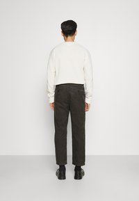 Vit tröja med rund halsringning, kombinerad med mörkbruna manchesterbyxor. Skorna är svarta och mörka strumpor syns. Ren och minimalistisk design.