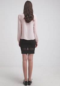 Blusa di seta rosa con maniche lunghe abbinata a una gonna a tubino nera aderente con un pannello in rete trasparente all'orlo.