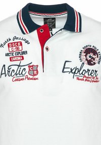 Polo blanco con cuello azul marino, tapeta de botones roja y texto y logotipos bordados del explorador ártico y la expedición al Polo Norte en rojo y azul marino.