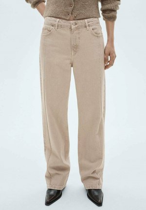 Beige wijde jeans met een hoge taille, voorzien van vier zakken en subtiele stikseldetails. Gekleed met elegante zwarte pumps.