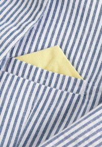 Tissu rayé blanc et bleu marine avec un mouchoir de poche jaune visible, présentant une finition texturée et des bords nets.