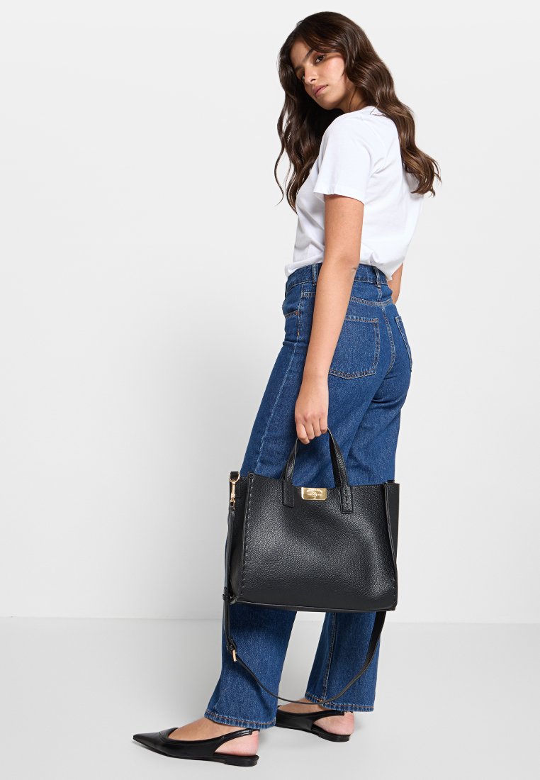 Bolso tote de cuero negro texturizado con asas cortas y correa para el hombro desmontable. Detalles en dorado y cremallera lateral visible.