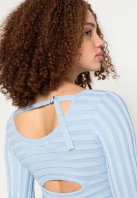 Top de lã azul claro com detalhes recortados nas costas e uma alça decorativa com um acabamento em metal. Textura suave e design ajustado.