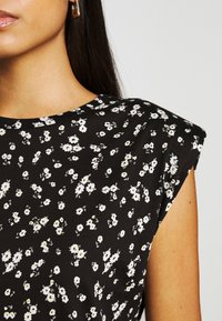 Haut floral noir avec un col rond, des manches courtes et un motif sans coutures de fleurs blanches avec des cœurs jaunes. Texture de tissu lisse.