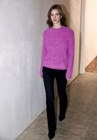 Różowy sweter dzianinowy z długimi rękawami, teksturowana tkanina, w zestawie z ciemnymi dżinsami i czarnymi botkami na obcasie, w minimalistycznym korytarzu.