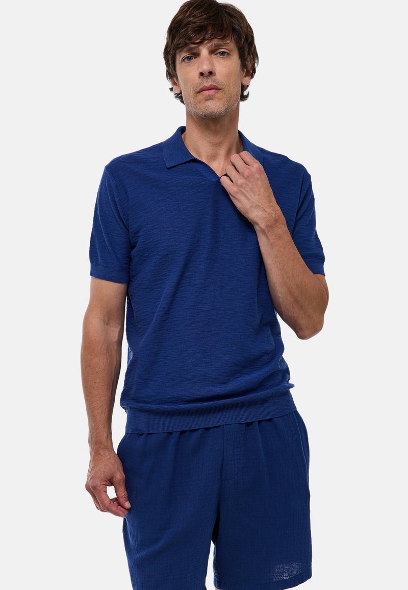 Polo en tricot bleu avec un col côtelé, des manches courtes et une coupe décontractée, associé à un short bleu assorti en tissu texturé.