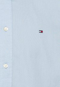 Camicia button-up azzurro chiaro in cotone; presenta un piccolo logo ricamato con accenti rosso, bianco e blu sul petto.