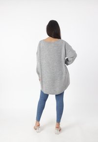 Overmaatse grijze trui met een brede necklijn en een geribbelde textuur, gecombineerd met blauwe skinny jeans en doorzichtige haksandalen.