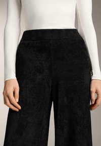 Čierne, mäkké, textúrované nohavice s širokým strihom a elastickým pásom, skombinované s bielym tričkom s dlhým rukávom. Zameranie na látku a strih.