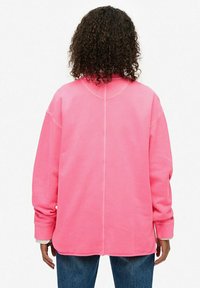 Sudadera de un color rosa brillante con un corte relajado, costuras visibles a lo largo del centro de la espalda y las mangas, cuello redondeado y puños acanalados.