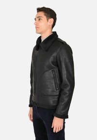 Giacca da pilota in pelle nera con colletto in pelliccia shearling, chiusura con zip, due tasche laterali e finitura testurizzata, che evidenzia un design robusto.