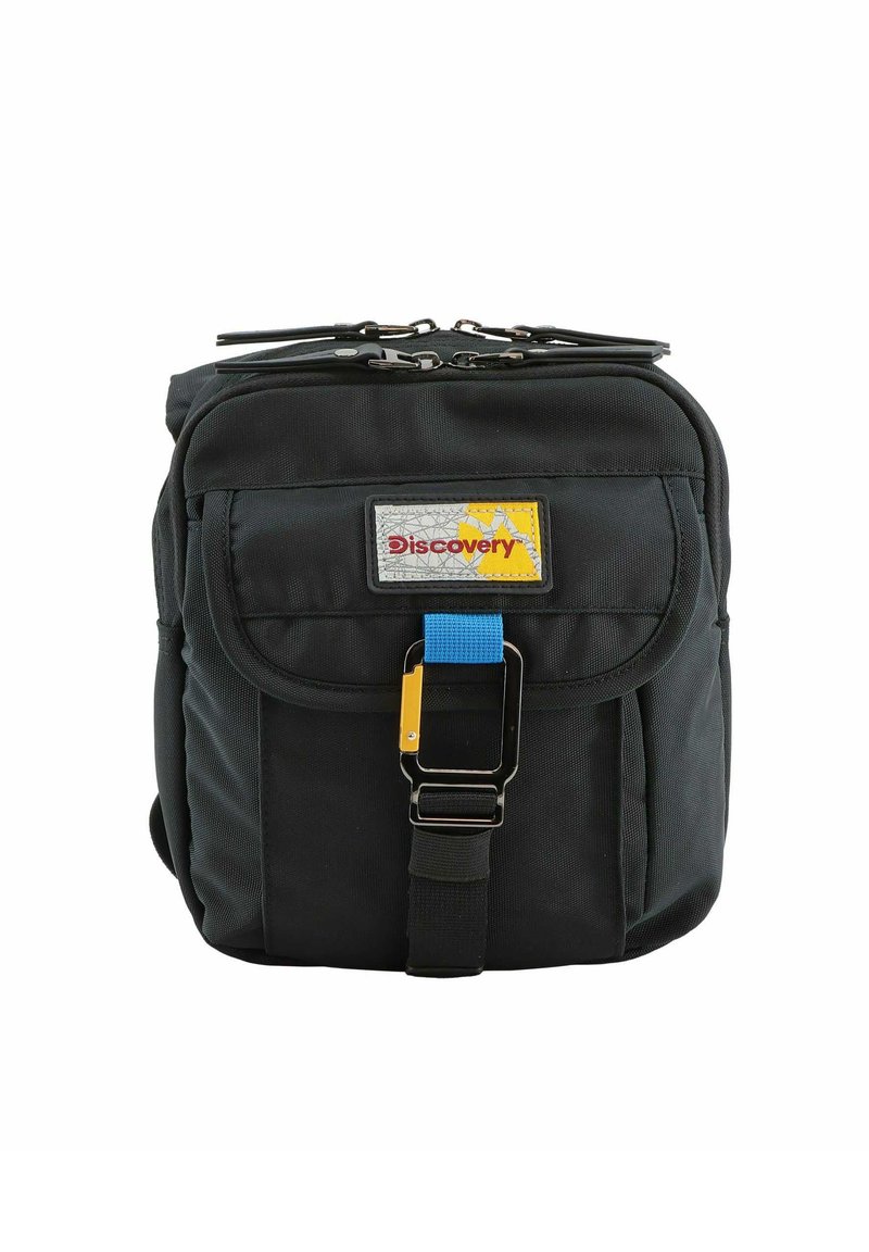 Mochila de tela negra con un bolsillo frontal, un parche de logo amarillo y gris, detalle de hebilla azul y cierres de doble cremallera en la parte superior.