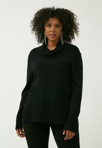 Schwarzer Rollkragenpullover mit gerippten Akzenten an den Bündchen, aus einem weichen Stoff mit lässigem Schnitt, kombiniert mit schwarzen Leggings.