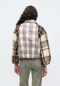 Mitme mustriga ruuduline jakk, millel on pruuni ja kreemjat tooni varjundid, krae ja elastsed varrukaservad. Kanditud oliivroheliste pükstega.