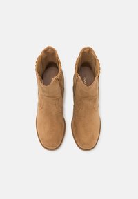Kávové semišové kotníkové boty s hladkým povrchem, kulatou špičkou a vlnitým okrajem na bocích. Obsahují polstrovanou stélku pro pohodlí.