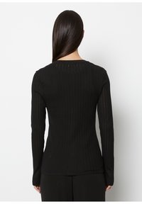 Black ribbed long-sleeve top with textured fabric, fitted design, and rounded neckline. Material has a slight sheen and shows horizontal stripes.
