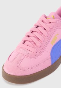 Rožiniai Puma sportbačiai su violetiniu šonu, auksiniu Puma logotipu, tekstūruotu padu ir tvirtai užrištomis rožinėmis šnūrėmis ant balto fono.