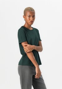 Mørkegrønn kortermet t-skjorte med rund hals og en avslappet passform, kombinert med grå slim-fit bukser. Glatt tekstur og minimalistisk design.