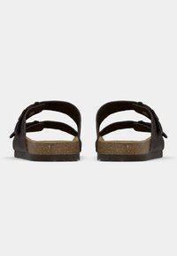 Καφέ σανδάλια τύπου slip-on με δύο ρυθμιζόμενα λουριά, υφή φελλού στο πέλμα και επίπεδη σόλα από καουτσούκ. Απλός σχεδιασμός με διακοσμητικές λεπτομέρειες.