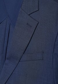 Blazer bleu marine en tissu texturé, avec un col cranté, une poche poitrine simple et une étiquette cousue sur la manche.