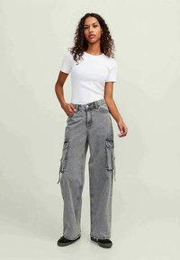 Calças cargo largas cinzentas com múltiplos bolsos laterais, uma cintura alta e um corte relaxado, acompanhadas de uma t-shirt branca ajustada.