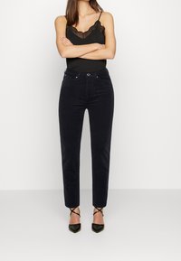 Svarta kordflöjtsbyxor med en figurnära silhuett, som har hög midja, framfickor och en mjuk yta. Matchas med svarta klackar.