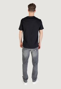 T-shirt en coton noir à manches courtes, associé à un jean en denim léger gris clair avec un design distinctif de poche arrière et un léger délavage.