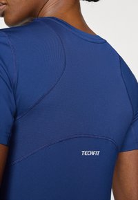 Camiseta deportiva ajustada de color azul marino con tejido texturizado, que presenta un escote redondo y el logo TECHFIT en la parte baja de la espalda.