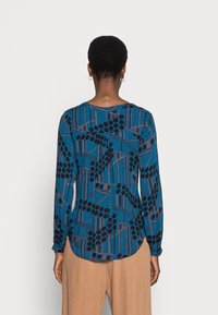 Langärmlige blaue Bluse mit abstrakten schwarzen und roten Mustern. Semislim Design mit einem runden Ausschnitt und gerafften Bündchen.