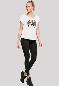 Bílý krátký rukáv T-shirt s multikolorovým grafickým logem Batmana, spárovaný s černými legínami a černými teniskami.