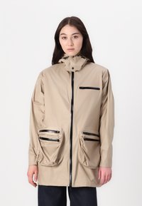 Beżowa wodoodporna kurtka z kapturem, z zamkiem z przodu, dwoma dużymi kieszeniami bocznymi oraz małą kieszonką na piersi z zamkiem.