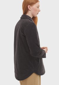 Dunkelgraue Cordjacke mit einem Kragen, langen Ärmeln und einem abgerundeten Saum. Verfügt über eine feine Textur und Seitentaschen.