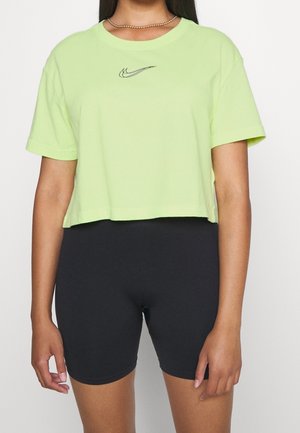 Zelené zkrácené tričko z bavlny, s krátkým rukávem a černým logem Nike uprostřed. V kombinaci s černými cyklistickými šortkami.