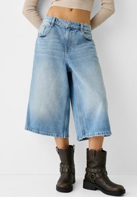 Ljusblå denim culotter med löst skuren passform, hög midja och rå fåll. Matchas med mörkbruna ankelstövlar med remmar och hårdvaruutskrifter.