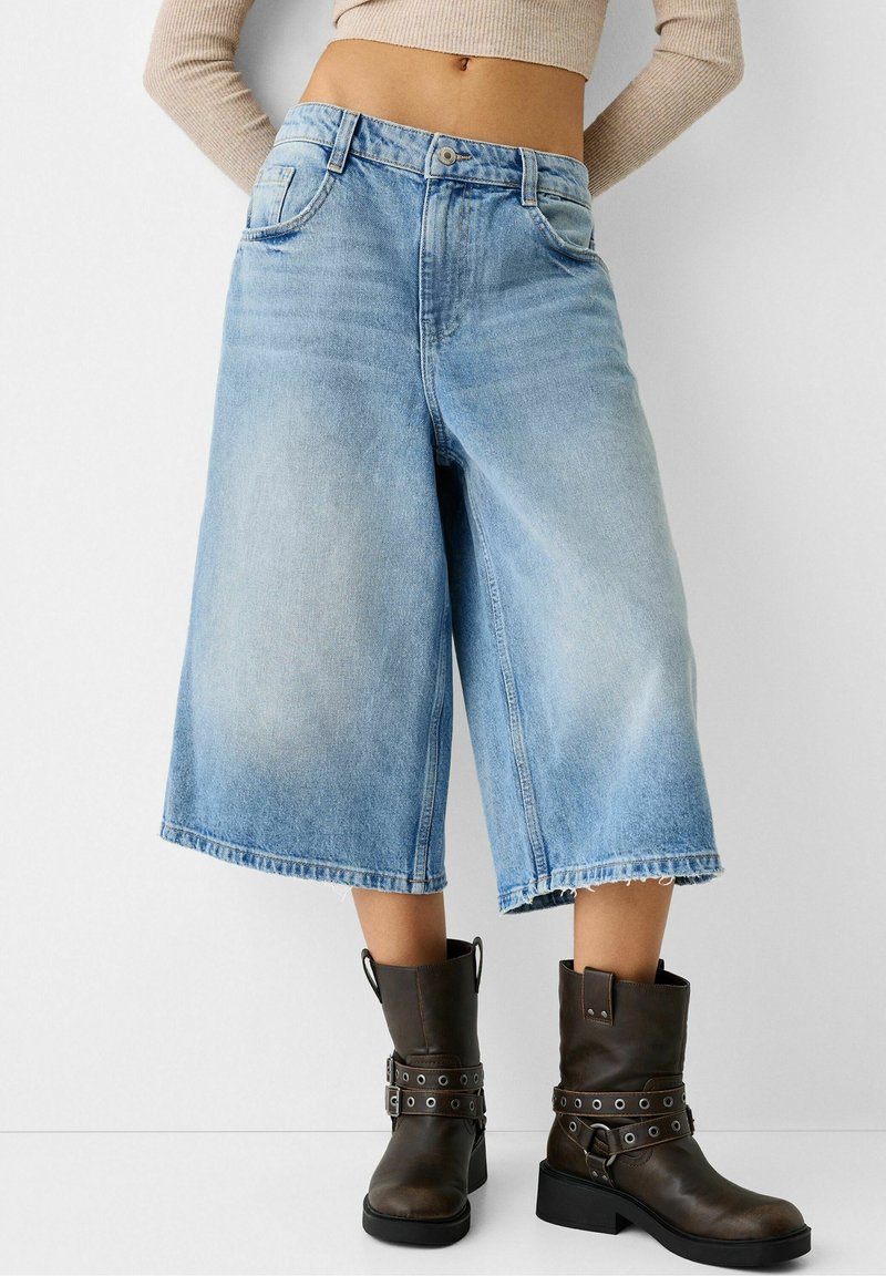 Ljusblå denim culotter med löst skuren passform, hög midja och rå fåll. Matchas med mörkbruna ankelstövlar med remmar och hårdvaruutskrifter.