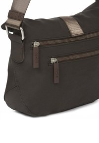 Bolso de hombro de tela marrón oscuro con dos bolsillos frontales con cremallera, herrajes plateados y una correa texturizada. Presenta un diseño minimalista y una textura suave.