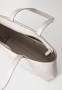 Borsa tote beige chiaro con due manici, apertura con zip e texture liscia; presenta una sottile rifinitura marrone e un ampio interno.